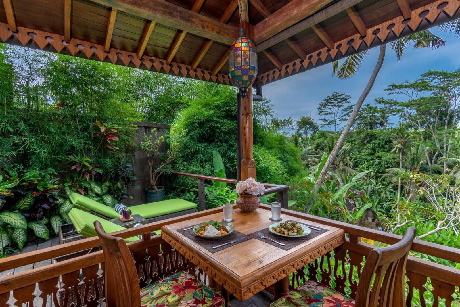A cottage veranda set for lunch under a carved timber roof, looking out over the jungle and rice terraces